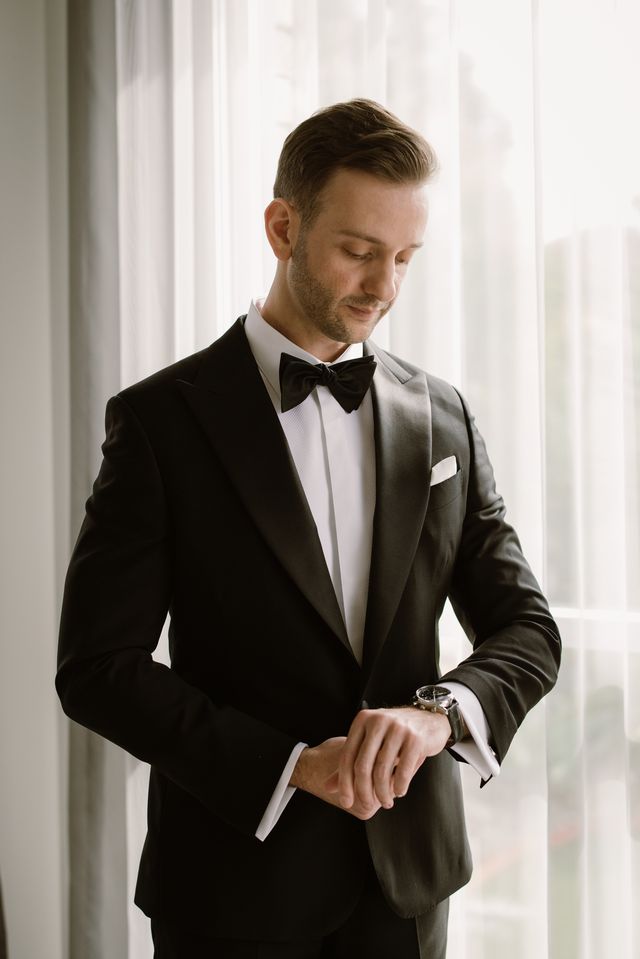 Groom in a black tuxedo adjusting his watch