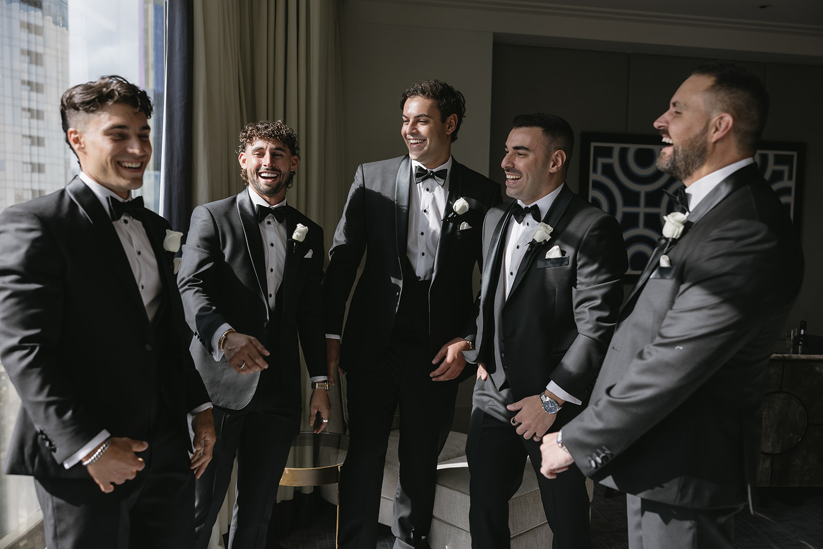 Groom and groomsmen in black-tie tuxedos sharing a laugh