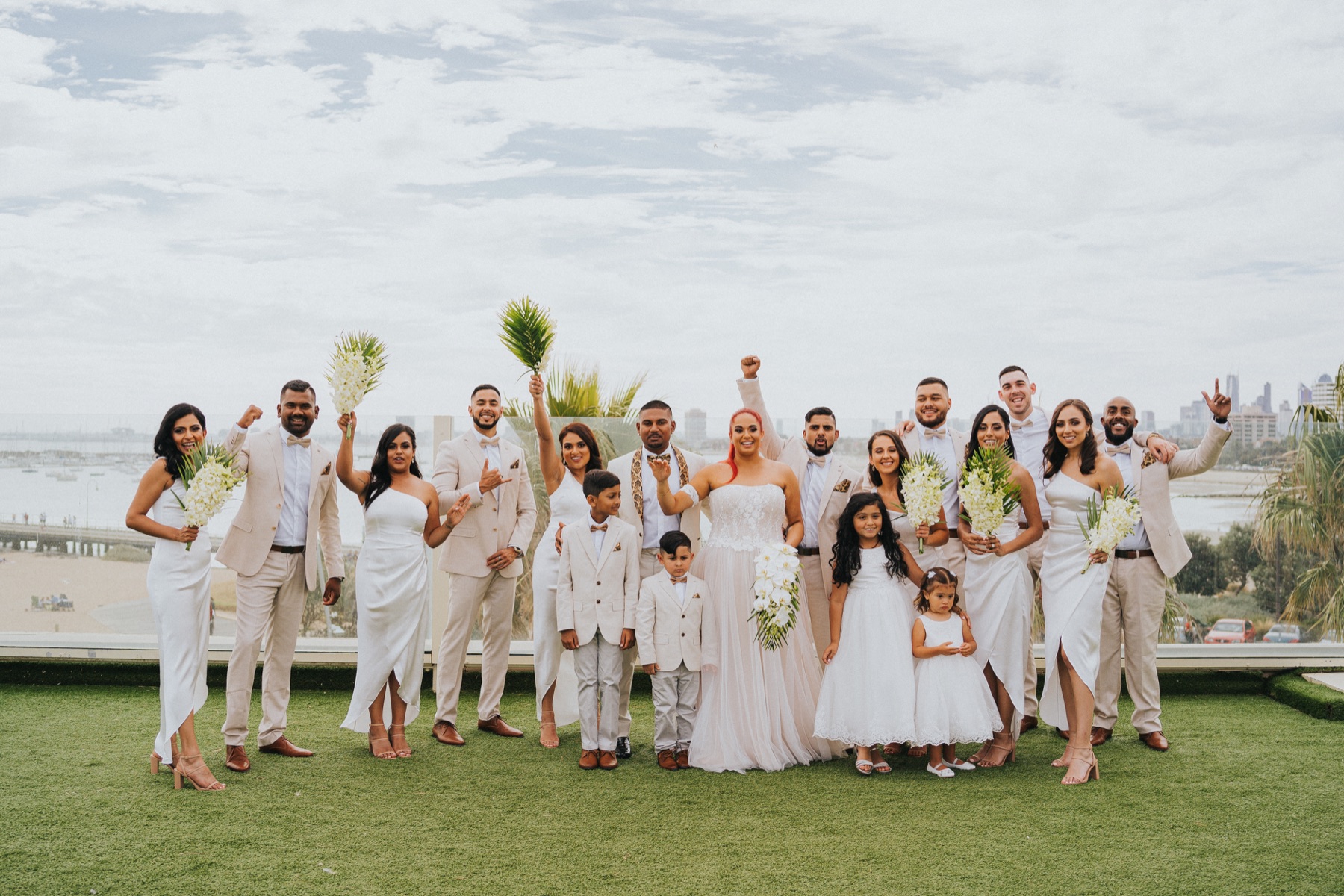 Full wedding party in tailored attire on a rooftop overlooking the bay